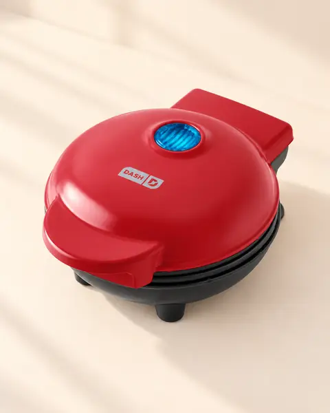 Red Dash mini waffle maker closed, with the indicator light on the lid